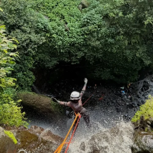 A canyoning participant rappelling down Curug Nangka Waterfall in Bogor, Indonesia, surrounded by lush rainforest during a guided adventure by Good Day.