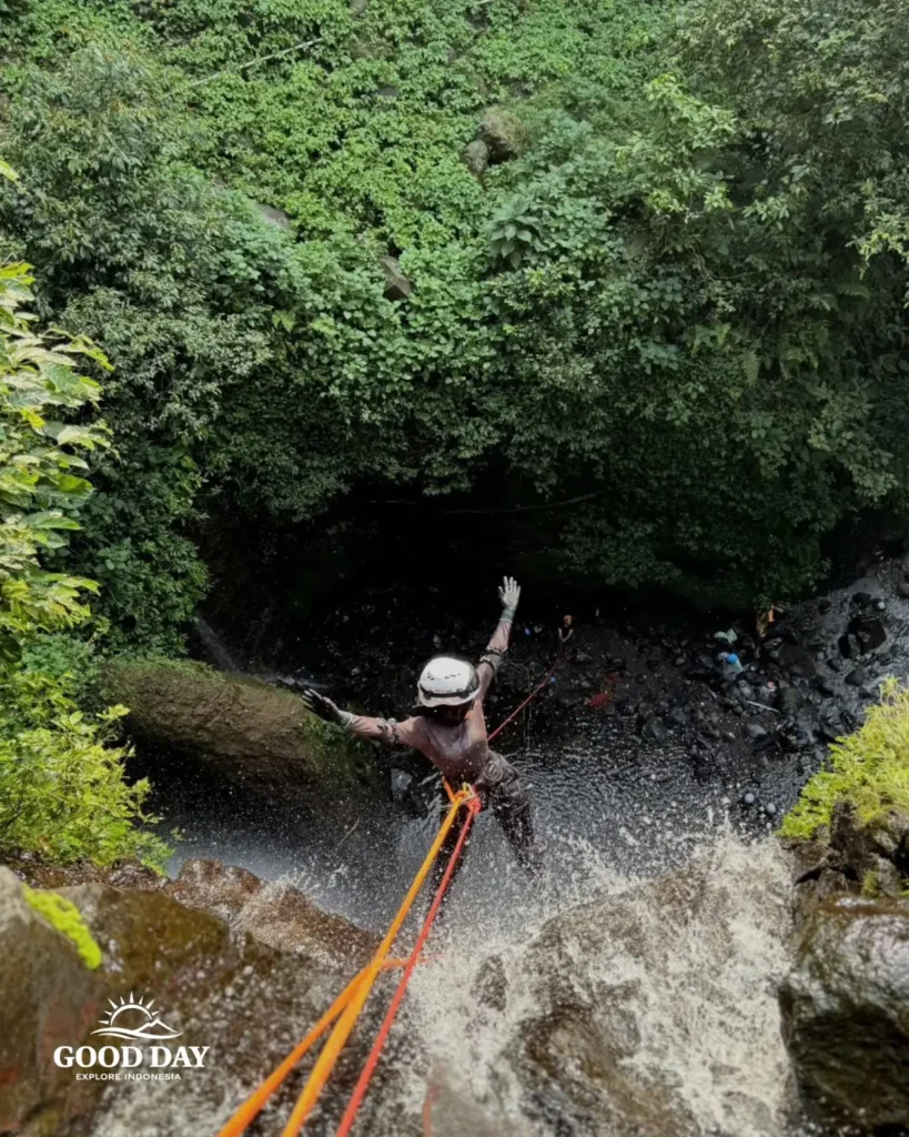 A canyoning participant rappelling down Curug Nangka Waterfall in Bogor, Indonesia, surrounded by lush rainforest during a guided adventure by Good Day.