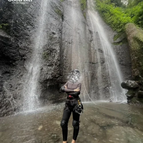 A canyoning participant rappelling down Curug Nangka Waterfall in Bogor, Indonesia, surrounded by lush rainforest during a guided adventure by Good Day.
