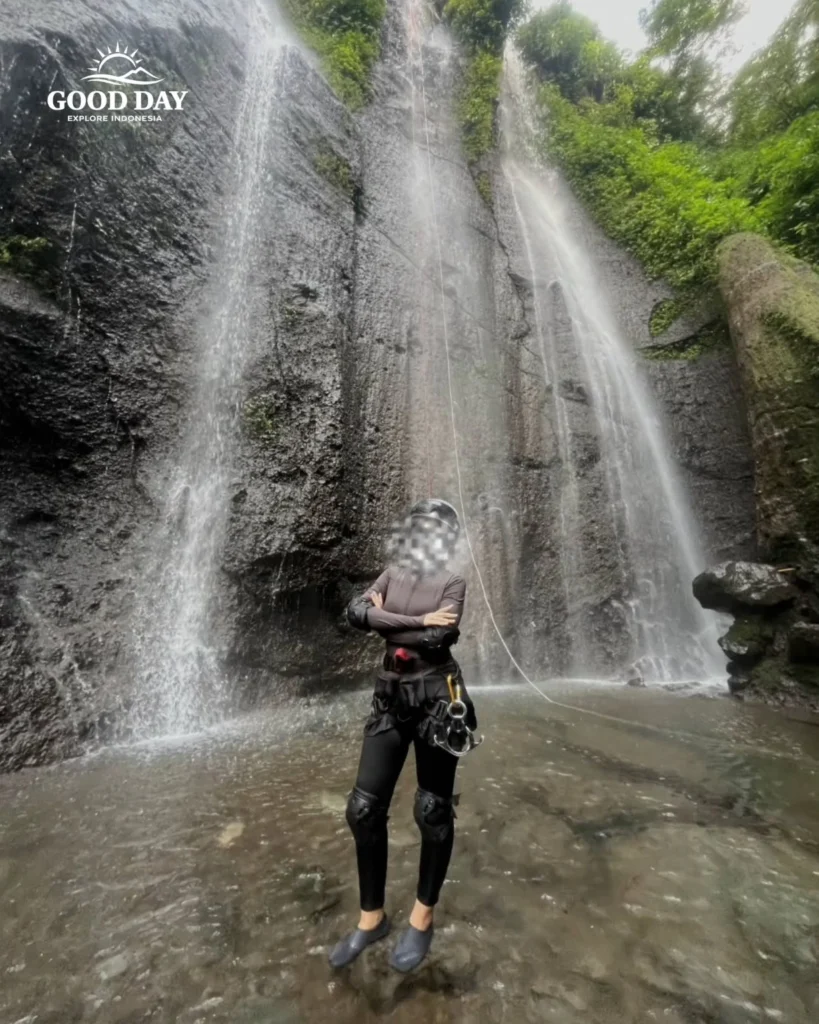 A canyoning participant rappelling down Curug Nangka Waterfall in Bogor, Indonesia, surrounded by lush rainforest during a guided adventure by Good Day.