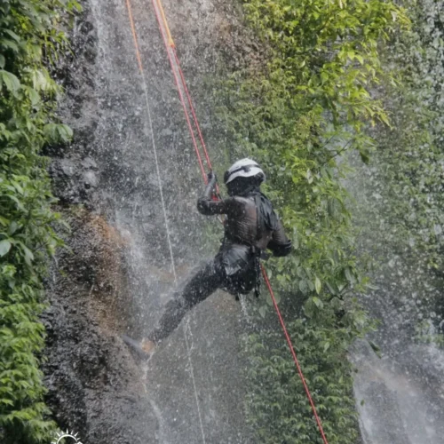 A canyoning participant rappelling down Curug Nangka Waterfall in Bogor, Indonesia, surrounded by lush rainforest during a guided adventure by Good Day.