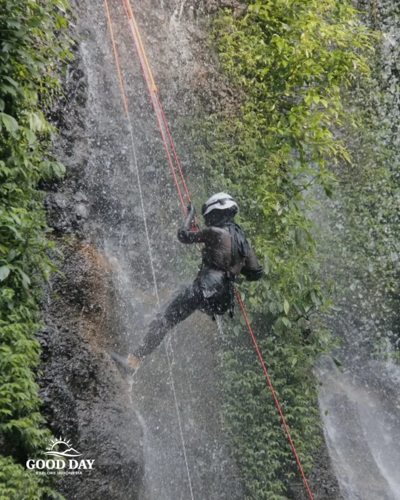 A canyoning participant rappelling down Curug Nangka Waterfall in Bogor, Indonesia, surrounded by lush rainforest during a guided adventure by Good Day.