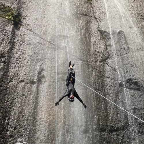 A canyoning participant rappelling down Curug Nangka Waterfall in Bogor, Indonesia, surrounded by lush rainforest during a guided adventure by Good Day.