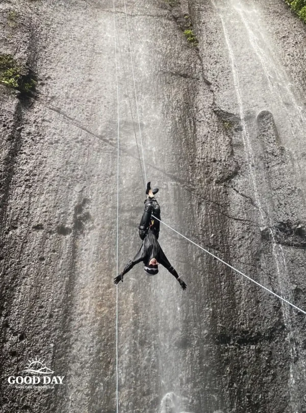 A canyoning participant rappelling down Curug Nangka Waterfall in Bogor, Indonesia, surrounded by lush rainforest during a guided adventure by Good Day.