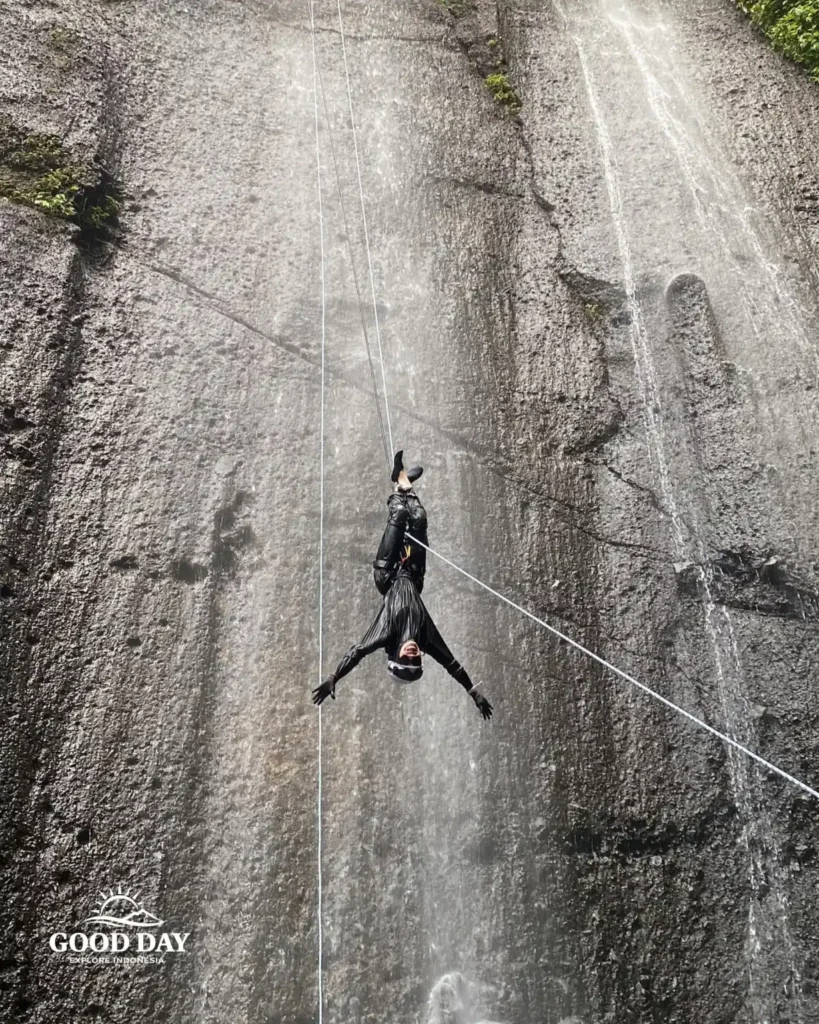 A canyoning participant rappelling down Curug Nangka Waterfall in Bogor, Indonesia, surrounded by lush rainforest during a guided adventure by Good Day.