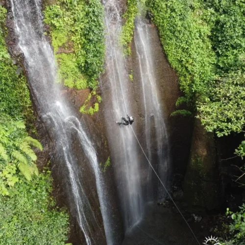 A canyoning participant rappelling down Curug Nangka Waterfall in Bogor, Indonesia, surrounded by lush rainforest during a guided adventure by Good Day.