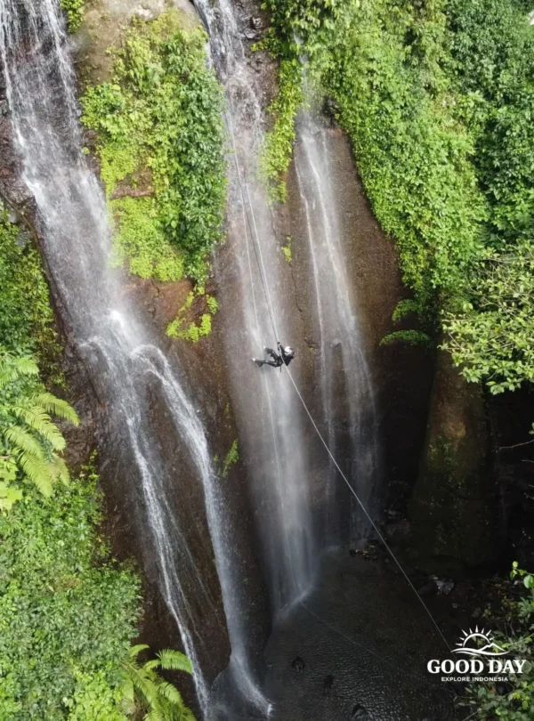 A canyoning participant rappelling down Curug Nangka Waterfall in Bogor, Indonesia, surrounded by lush rainforest during a guided adventure by Good Day.