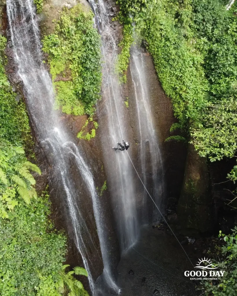 A canyoning participant rappelling down Curug Nangka Waterfall in Bogor, Indonesia, surrounded by lush rainforest during a guided adventure by Good Day.