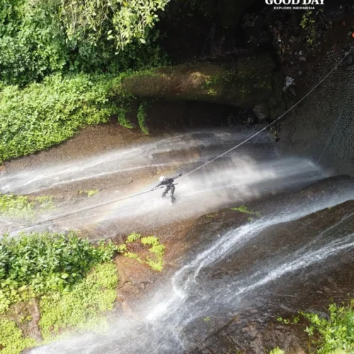 A canyoning participant rappelling down Curug Nangka Waterfall in Bogor, Indonesia, surrounded by lush rainforest during a guided adventure by Good Day.