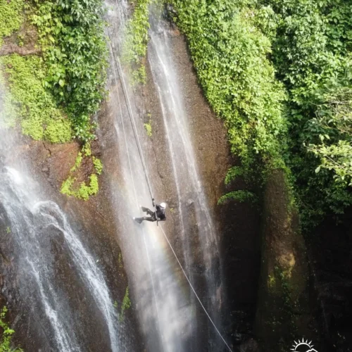 A canyoning participant rappelling down Curug Nangka Waterfall in Bogor, Indonesia, surrounded by lush rainforest during a guided adventure by Good Day.