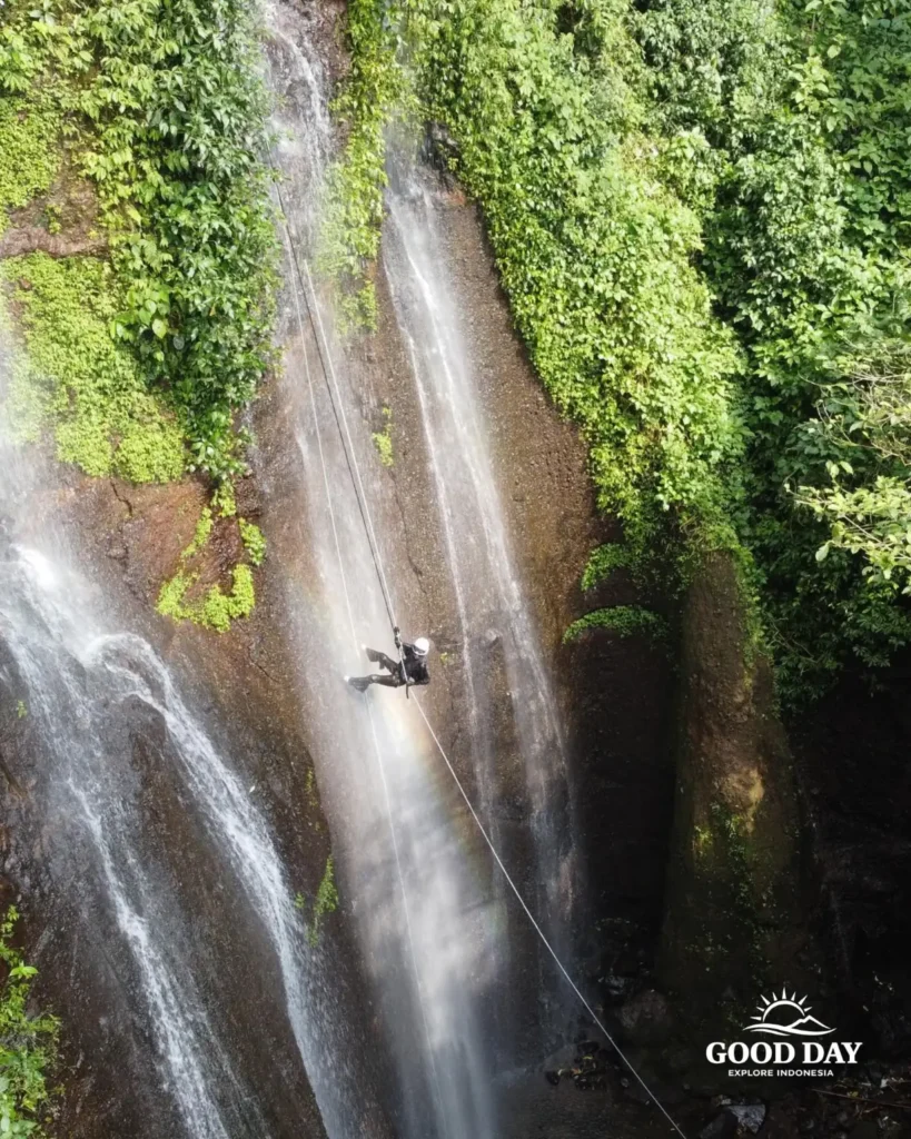 A canyoning participant rappelling down Curug Nangka Waterfall in Bogor, Indonesia, surrounded by lush rainforest during a guided adventure by Good Day.