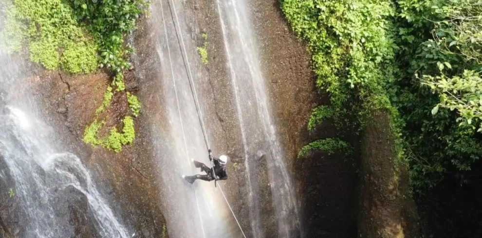A canyoning participant rappelling down Curug Nangka Waterfall in Bogor, Indonesia, surrounded by lush rainforest during a guided adventure by Good Day.